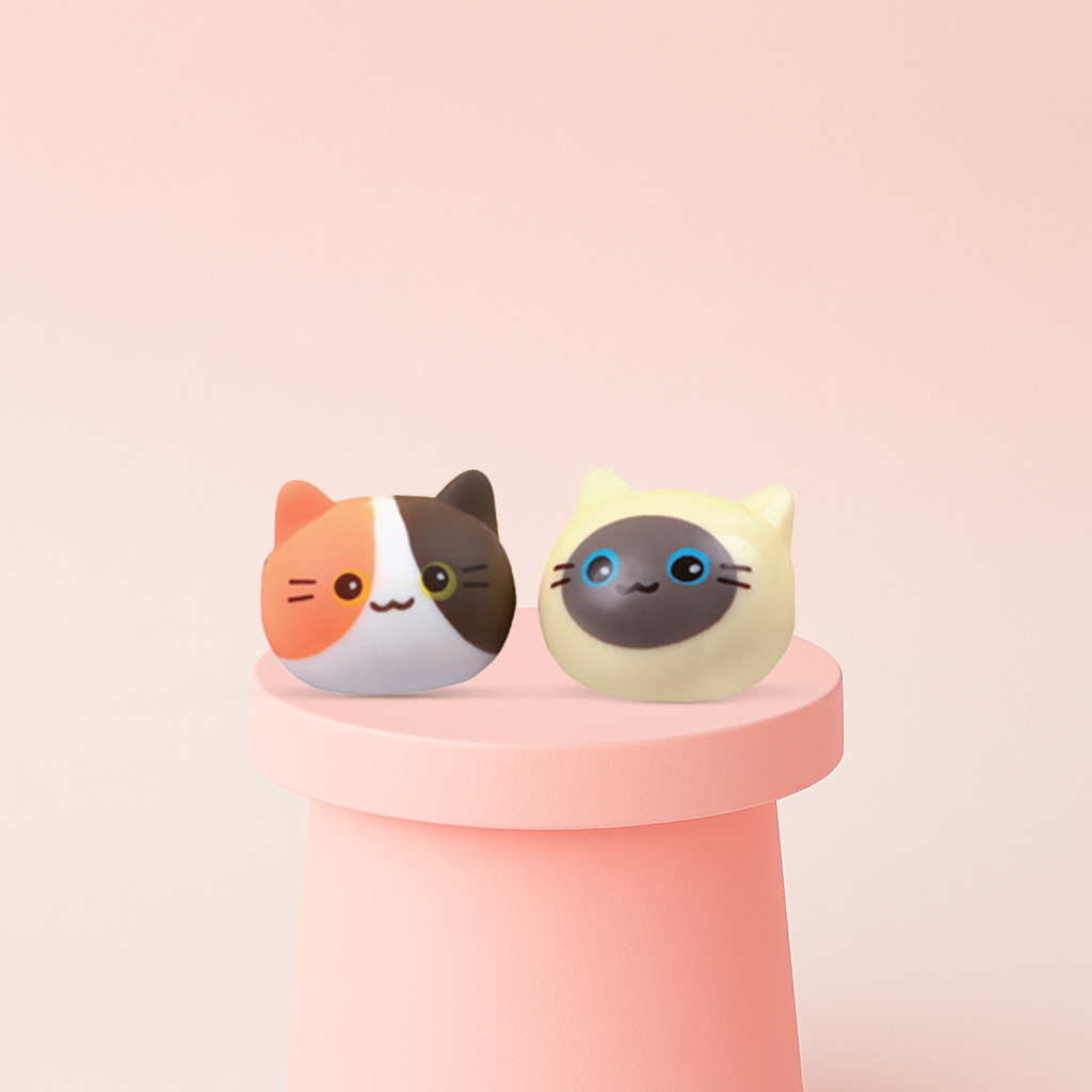 Two cat-shaped squishies on a pink stand with a light pink background